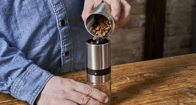 Kaffeebohnen werden in Handmühle gefüllt um gemahlen zu werden