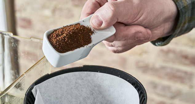 Kaffeepulver wird in Papierfilter in Kaffeemaschine gefüllt
