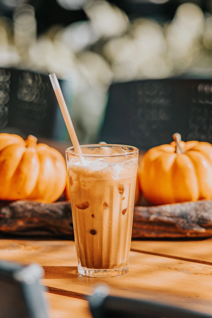 Iced Pumpkin Spice Latte in hohem Glas mit Kürbis Dekoration im Hintergrund