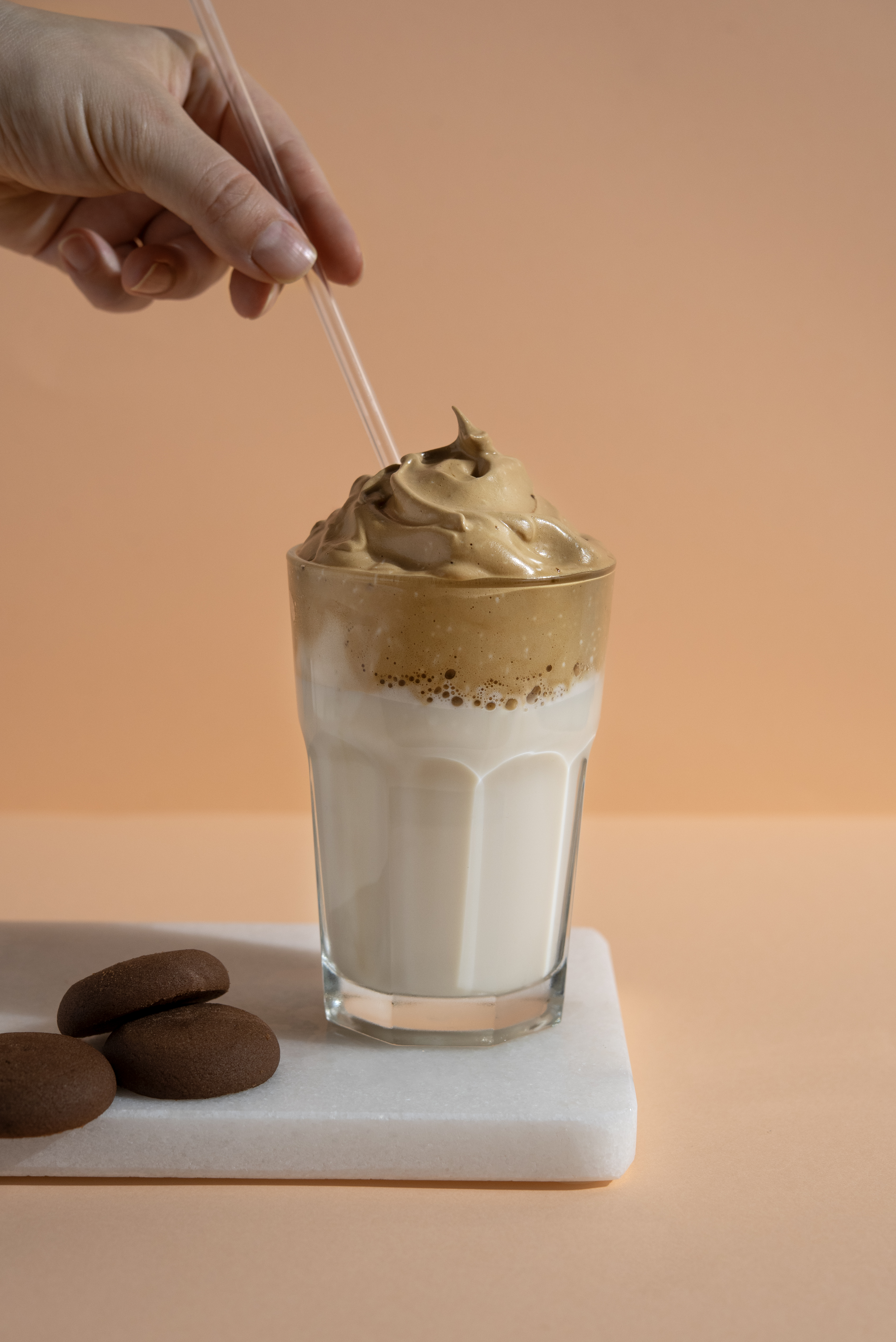 Aufgeschäumter Kaffee im Glas mit Keksen daneben.