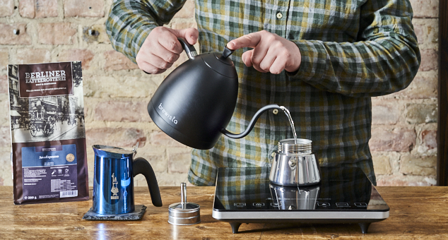 Mann füllt heißes Wasser in blaue Espresso Herdkanne von Bialetti