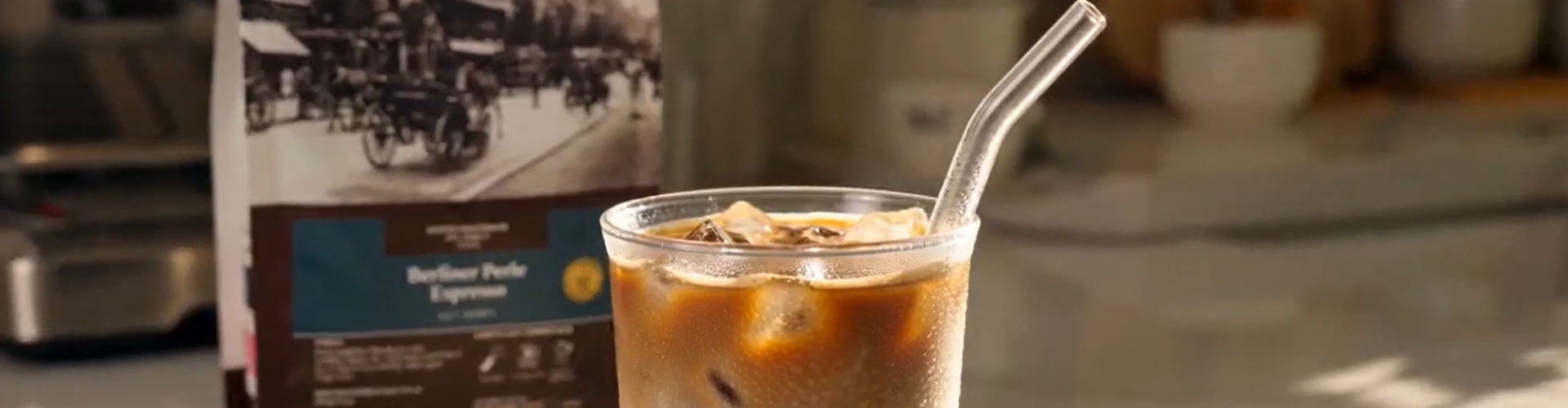 Berliner Kaffeerösterei Kaffeerezept Eiskaffee Sommer mit Espresso und Eiswürfeln Iced Latte im Becher mit Strohhalm - Hintergrund