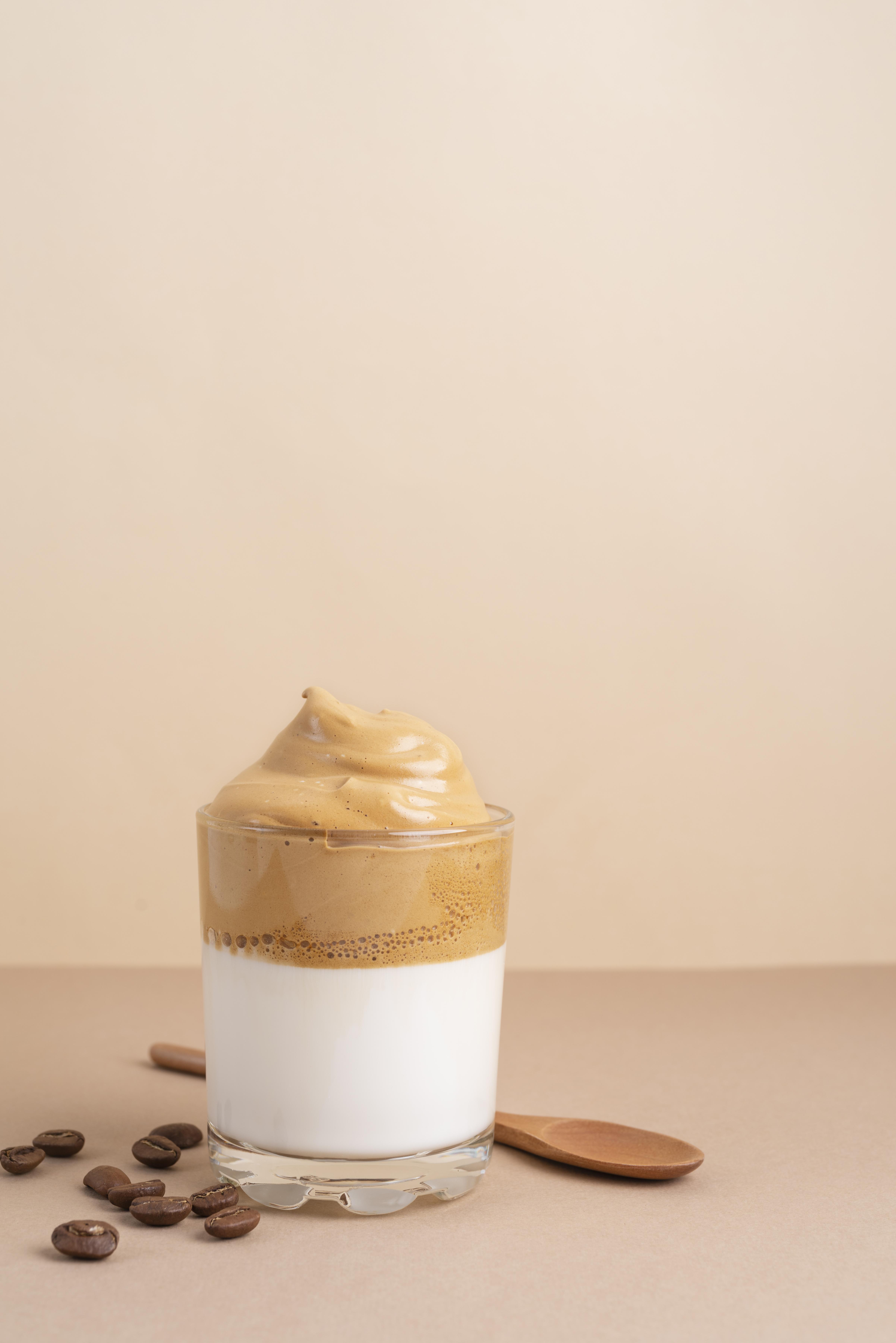 Dalgona Coffee Aufgeschäumter Kaffee im Glas. Kaffeebohnen und eine Glasflasche mit Milch im Hintergrund