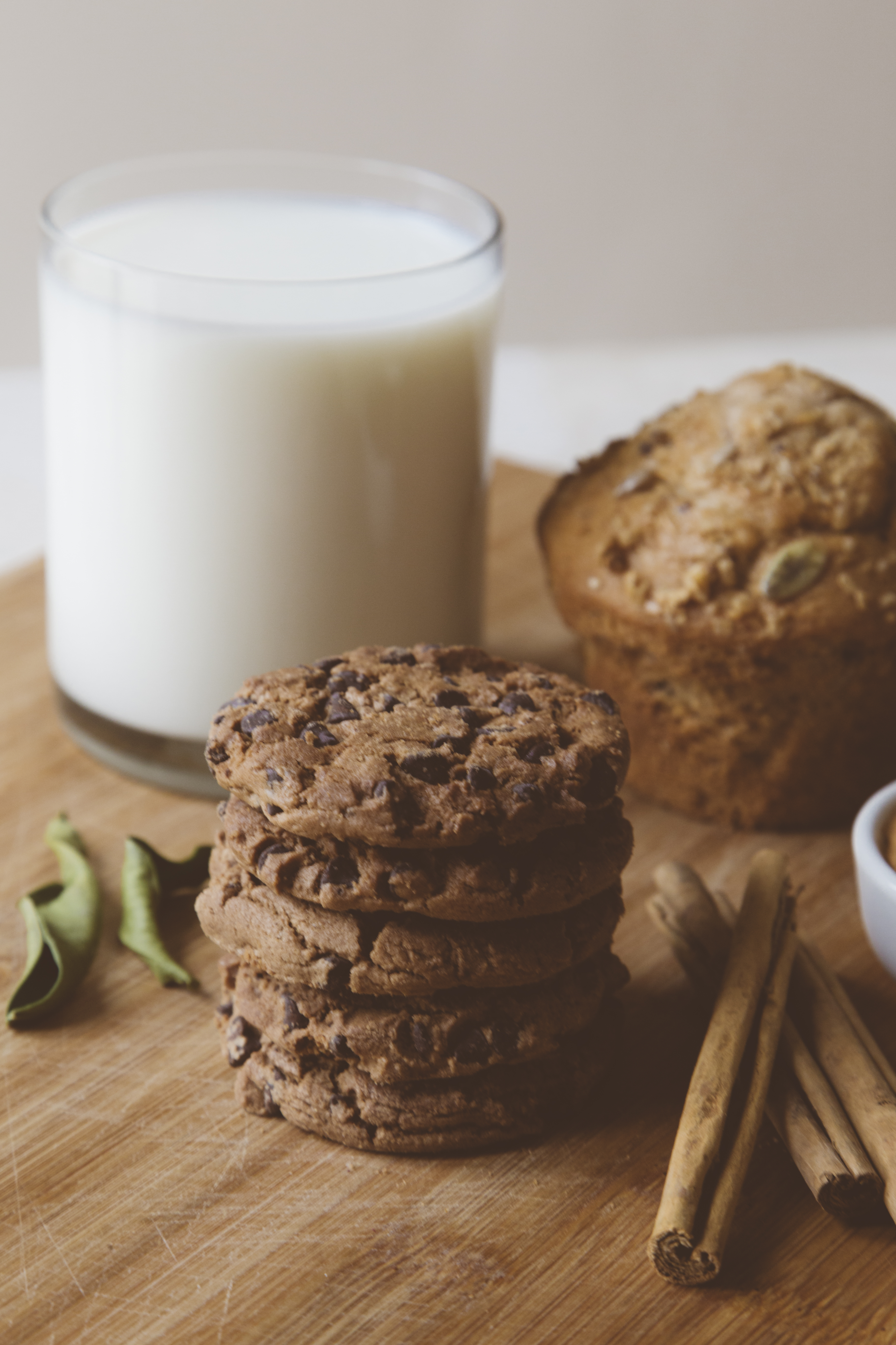 5 Chocolate Chip Cookies aufeinander gestapelt auf einem Brett mit Milch, einem Muffin und mit im Hintergrund.