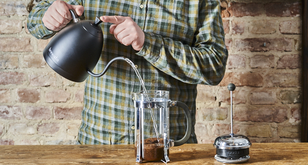 Mann gießt heißes Wasser in French Press mit Kaffeepulver