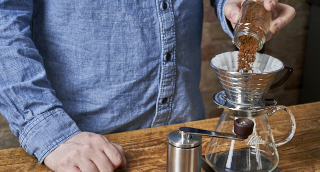 Kaffeepulver wird in Kalita Handfilter mit Kalita Papierfilter gefüllt mit Handmühle im Vordergrund