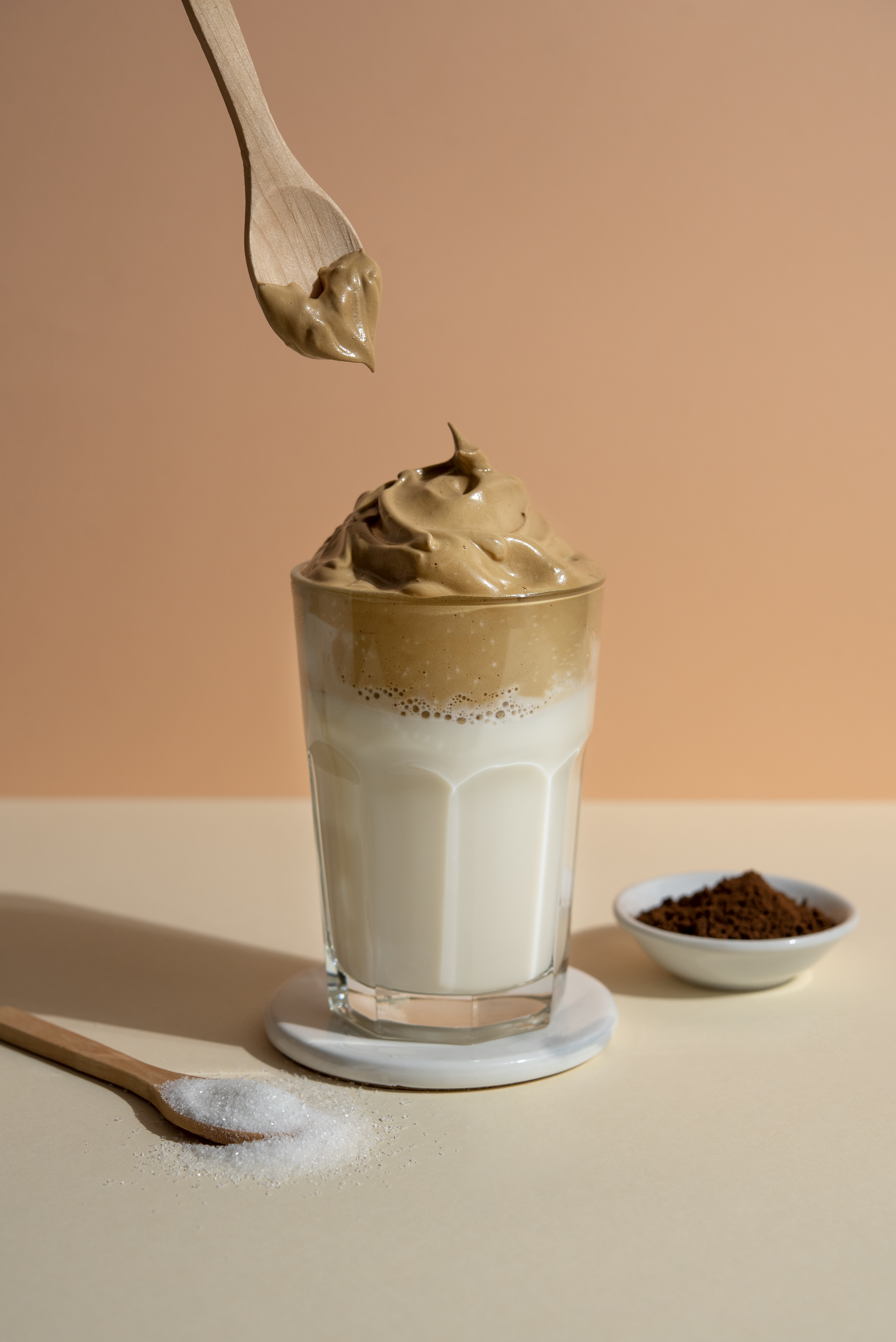 Aufgeschäumter Kaffee im Glas. Zucker und Instant Coffee im Hintergrund