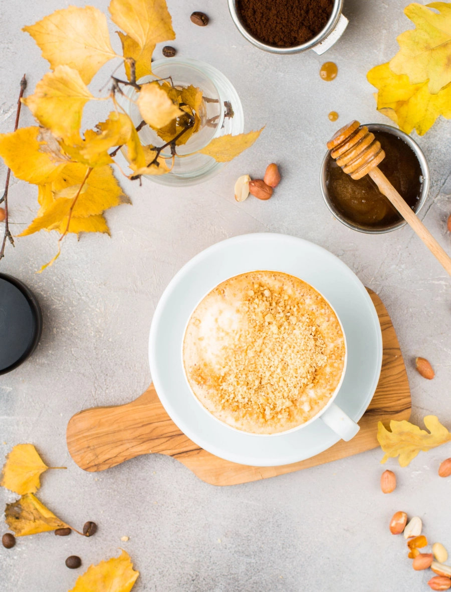 Cappuccino in einer großen Tasse mit Honig und goldenen herbstlichen Blättern